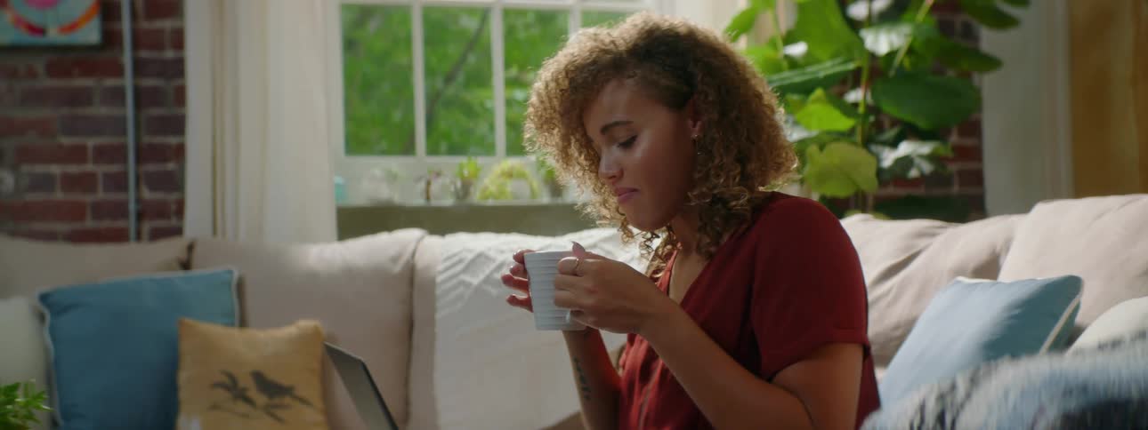 A young woman drinking coffee at home while sitting on the couch
