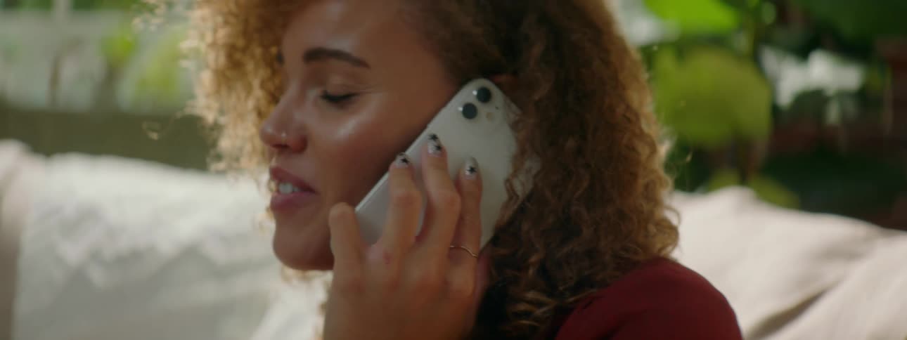 A young woman sits on a couch talking on a cell phone