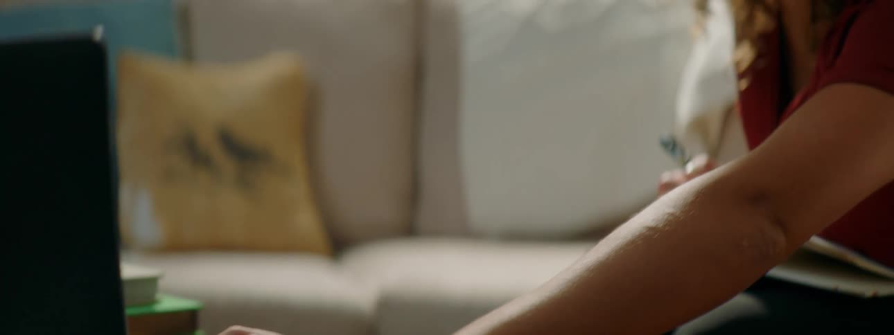 A teenage girl sitting on a couch at home uses a laptop
