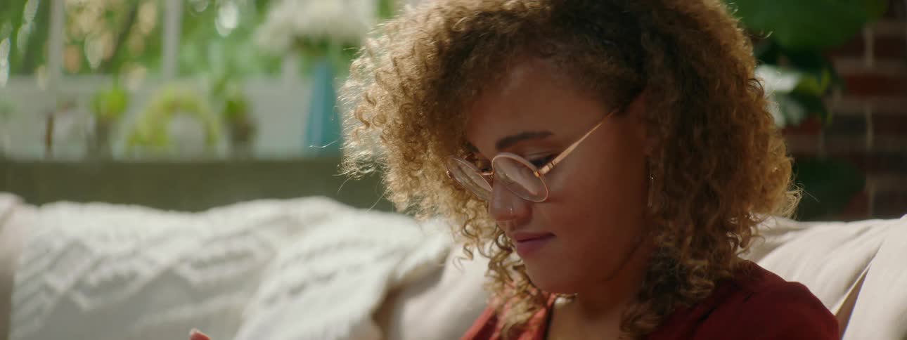 Woman with red curly hair and a red shirt sits on a sofa and uses a tablet