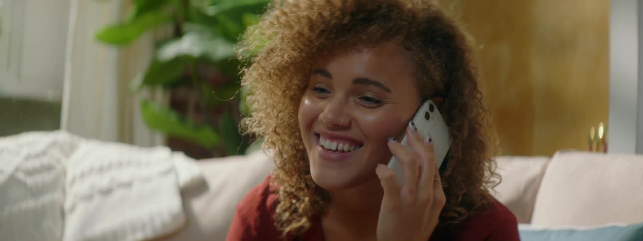A teenage girl sitting at home picks up her cell phone and talks