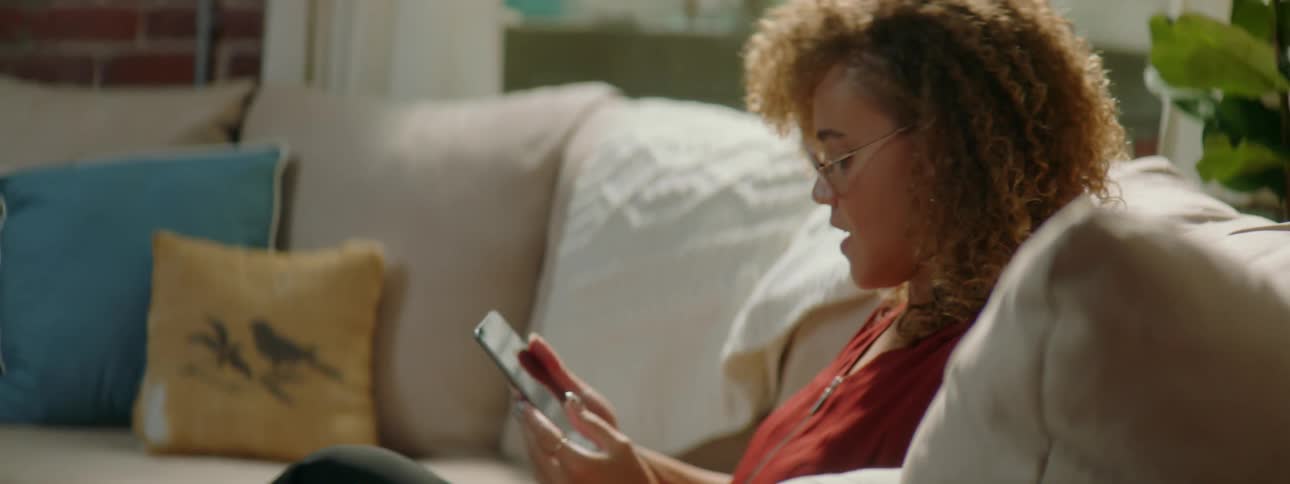 Young woman picks up a tablet and sits on a couch at home