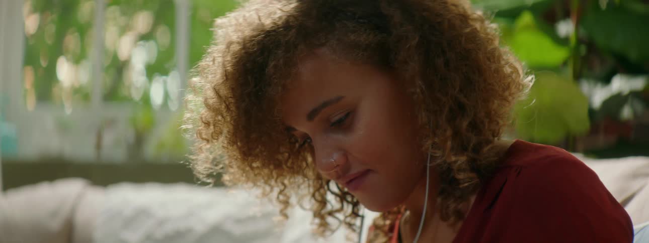 Woman with red curly hair wearing earphones and uses a smartphone in a living room