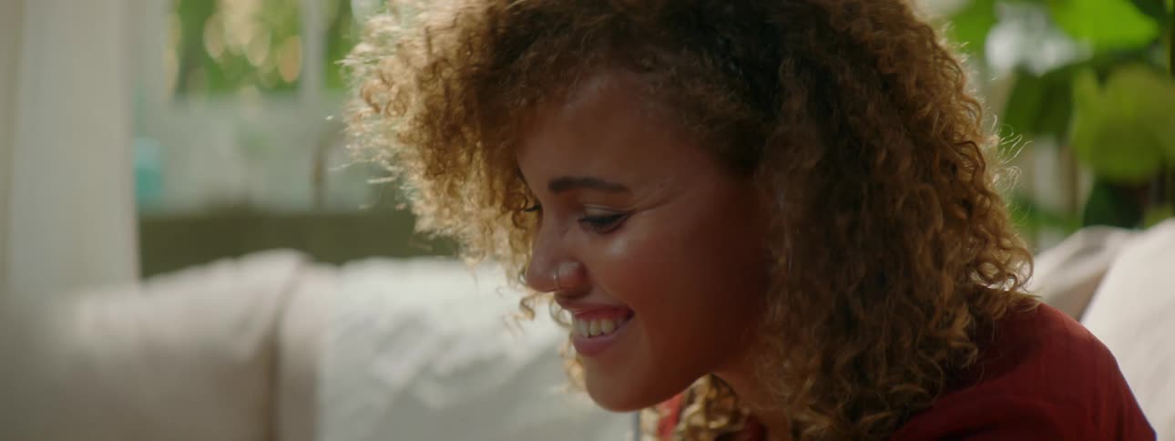 Woman with red curly hair and a red blouse makes a video call on the smartphone in the living room at home