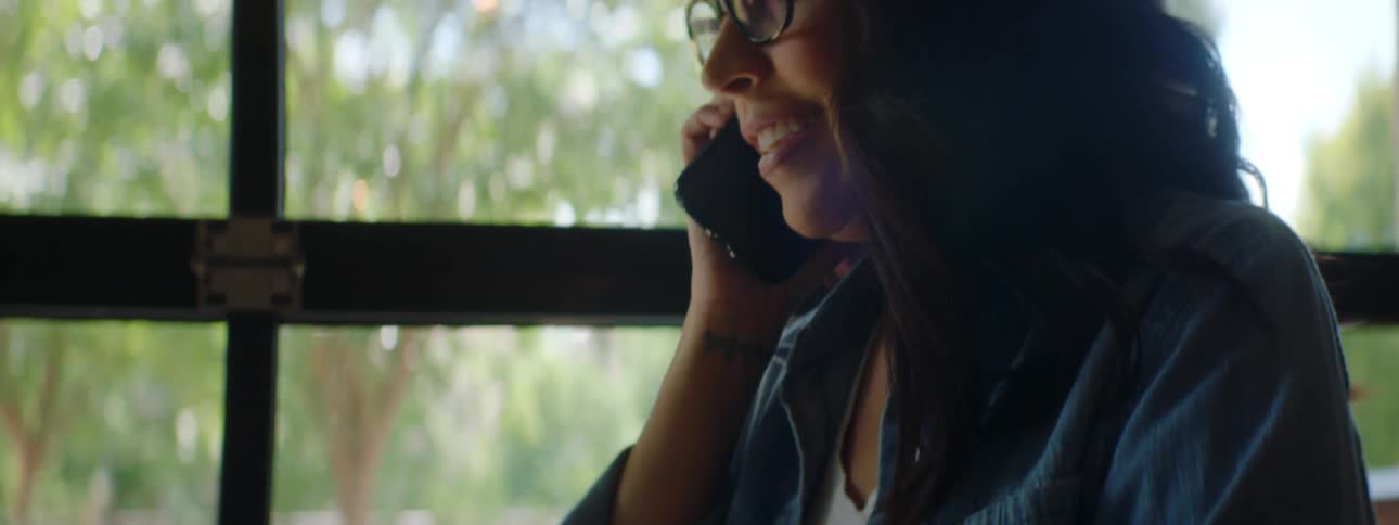 A woman types on a laptop while speaking on a cell phone