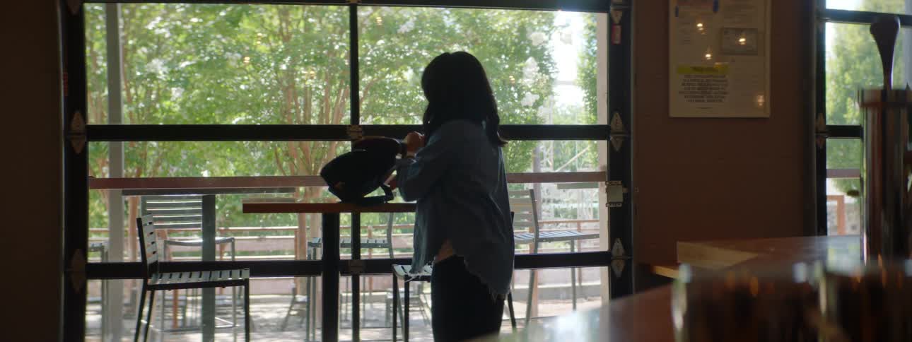 A woman enters a cafe and removes her laptop from her bag to place it on a table