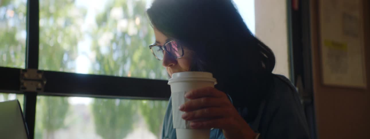 A woman receives a drink sitting at a cafe table with a laptop
