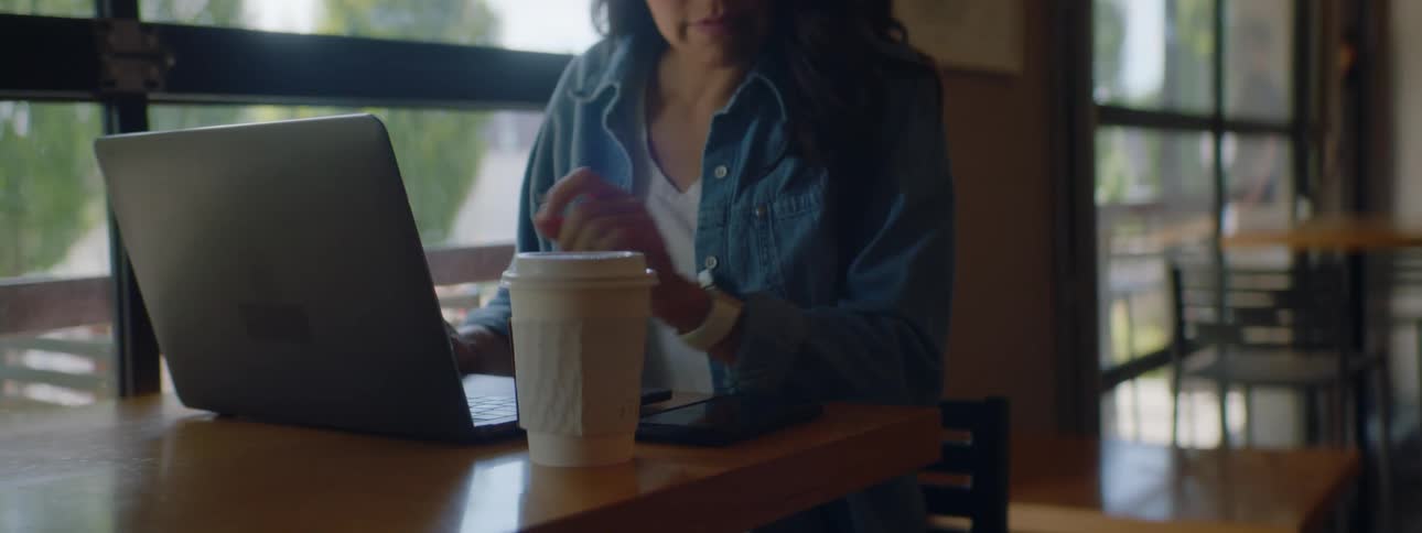 A woman sits in a cafe with a laptop then answers her cell phone and smiles