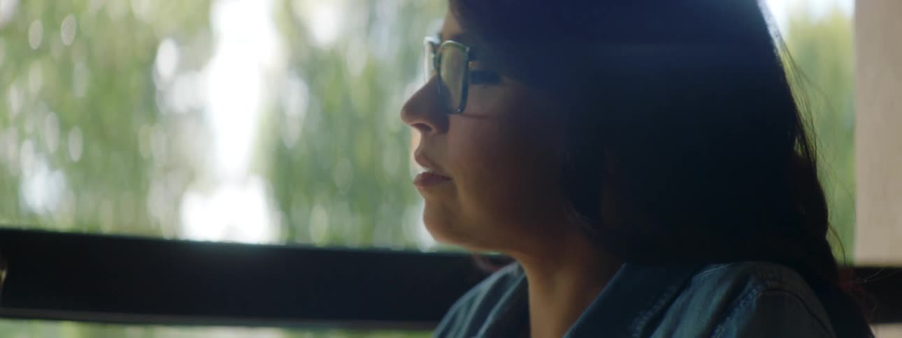A woman tapping on the keys of a laptop pauses and looks out the window then around