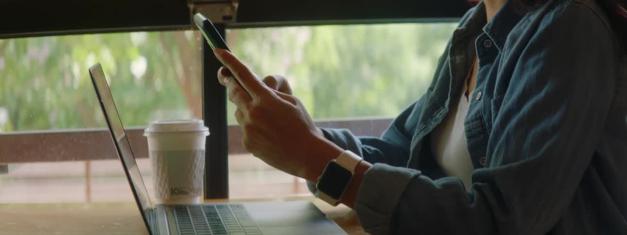 Woman with wavy hair and glasses sits at a table and uses a smartphone in a cafe