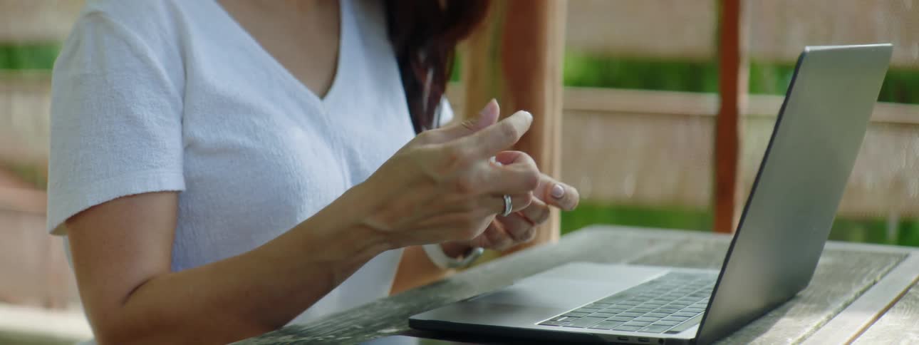A woman fiddles with an object while sitting at a table with a laptop