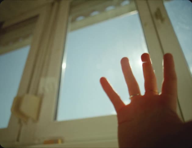 A woman holds her hand in front of a window so the sunlight can reflect off the rings she is wearing