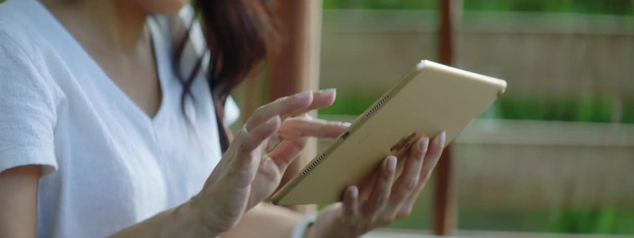 A woman swipes on the screen of a tablet while sitting outdoors during the day