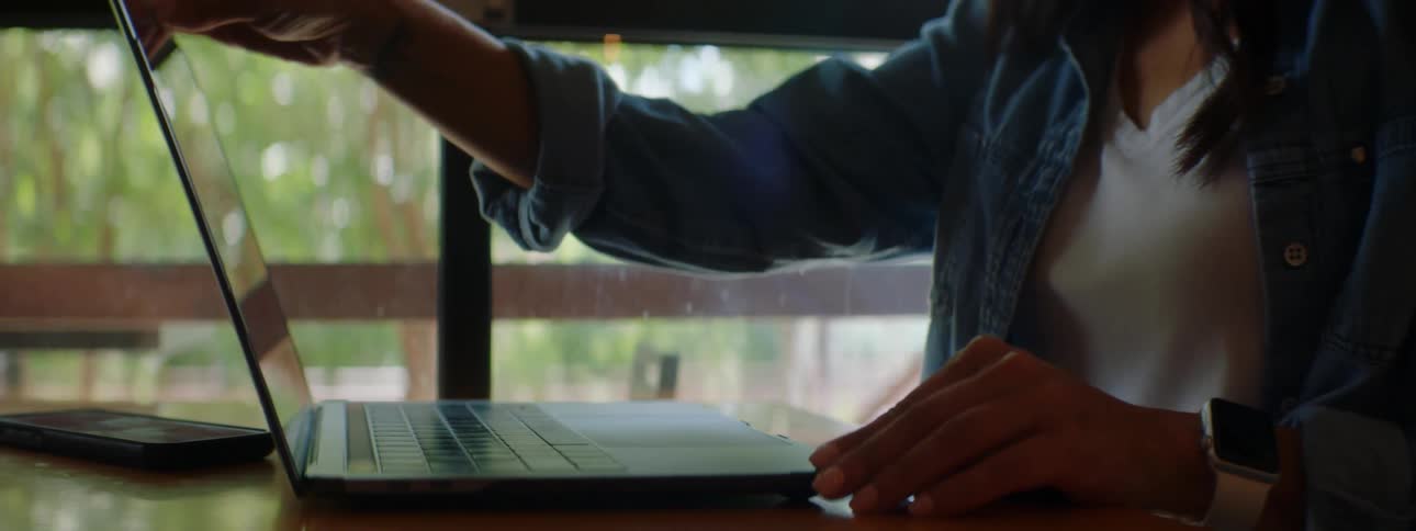 Woman sitting at table opens laptop and begins typing