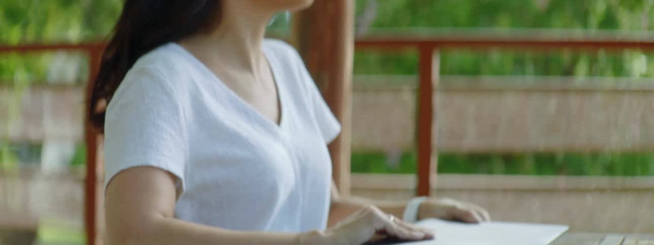 Brunette woman with wavy hair and a white shirt puts a tablet and takes out a laptop from her bag
