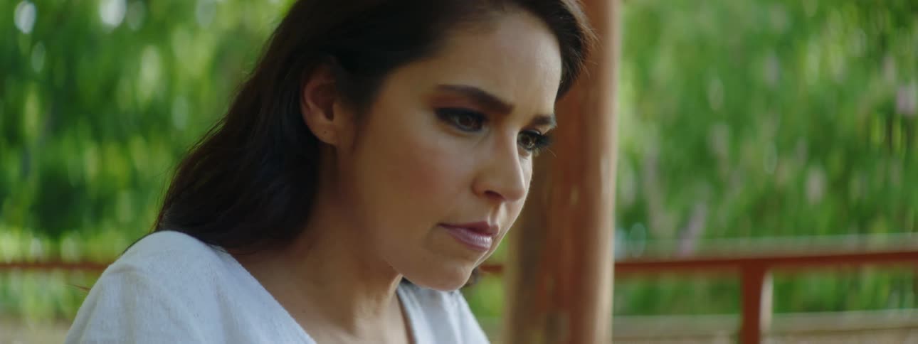 A woman sits outside and types on a laptop with a contemplative expression on her face