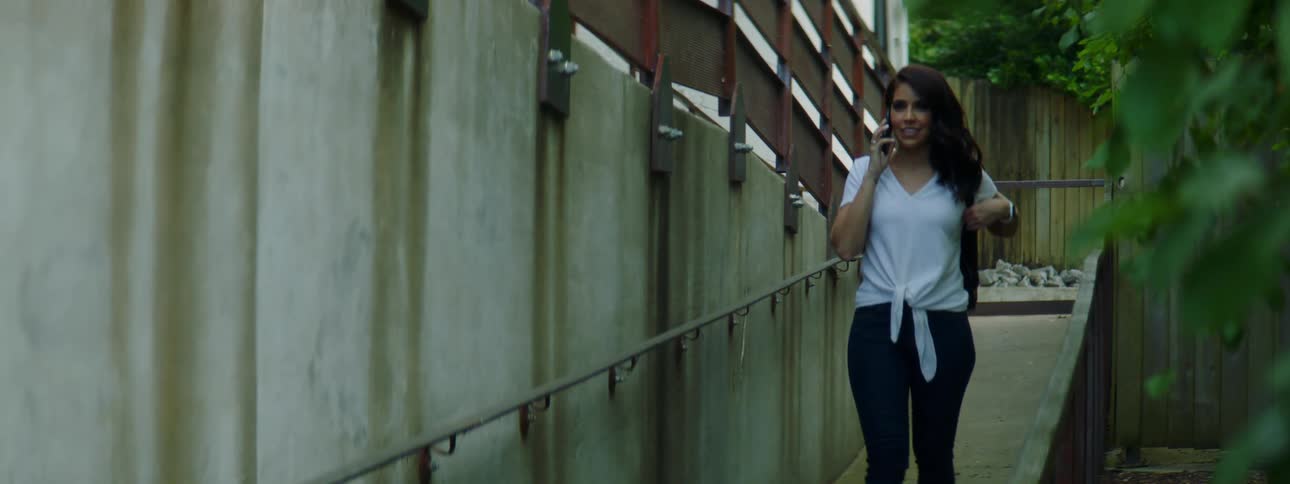 A young woman walking outside makes a phone call and talks on her cell phone
