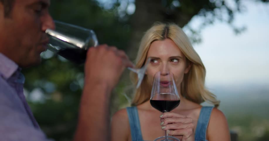 A young woman and a man drink glasses of wine while standing outdoors during the day