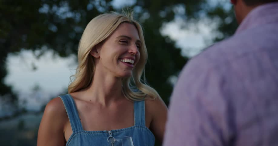 Young woman smiles and laughs while talking to man outdoors