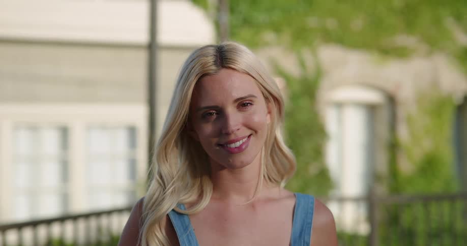 Blonde woman with long hair faces the camera with eye contact and smiles broadly