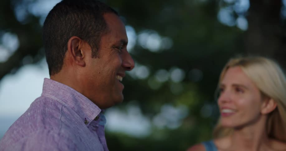 A man and a woman standing and talking with trees and the sky in the background