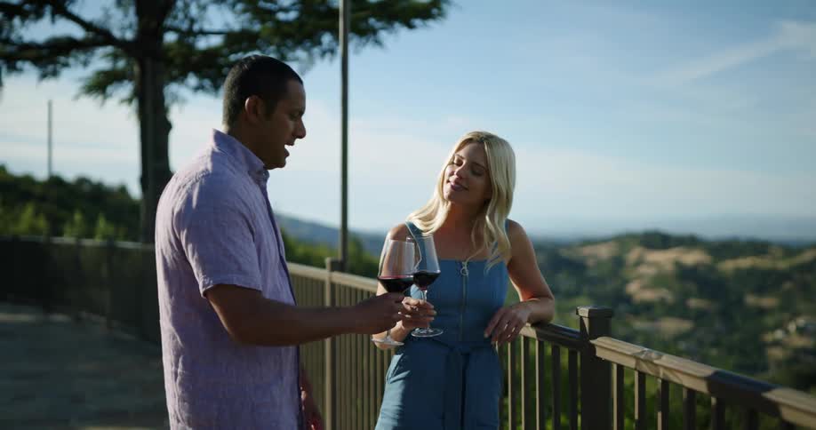 Couple drink red wine on a date next to a banister looking at the hills