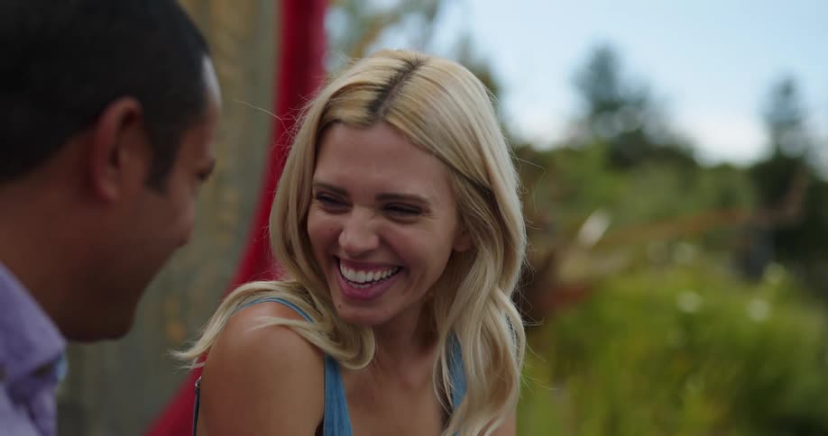 A blonde haired woman sits next to a male companion and laughs heartily