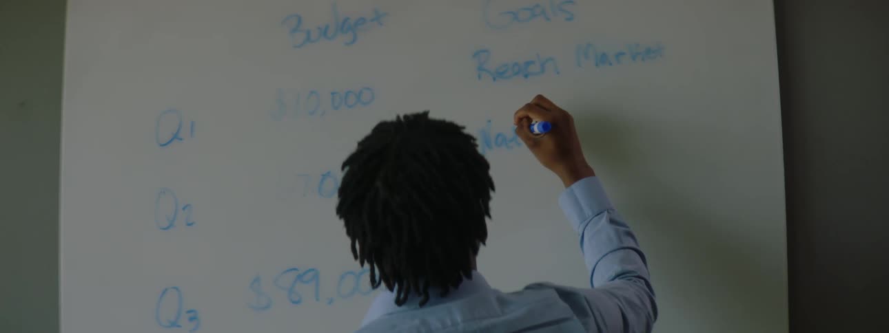 A man uses a blue marker to draw a table on a whiteboard