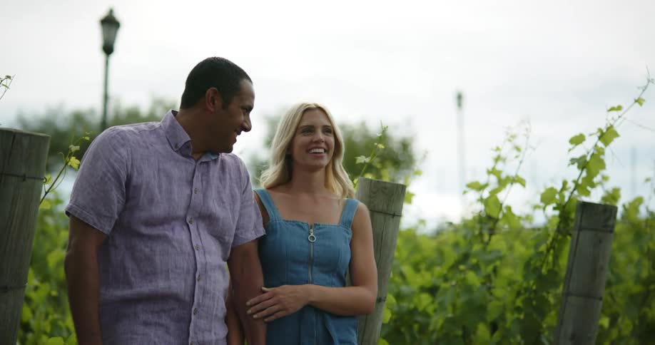 A man and a woman holding hands and walking in a vineyard