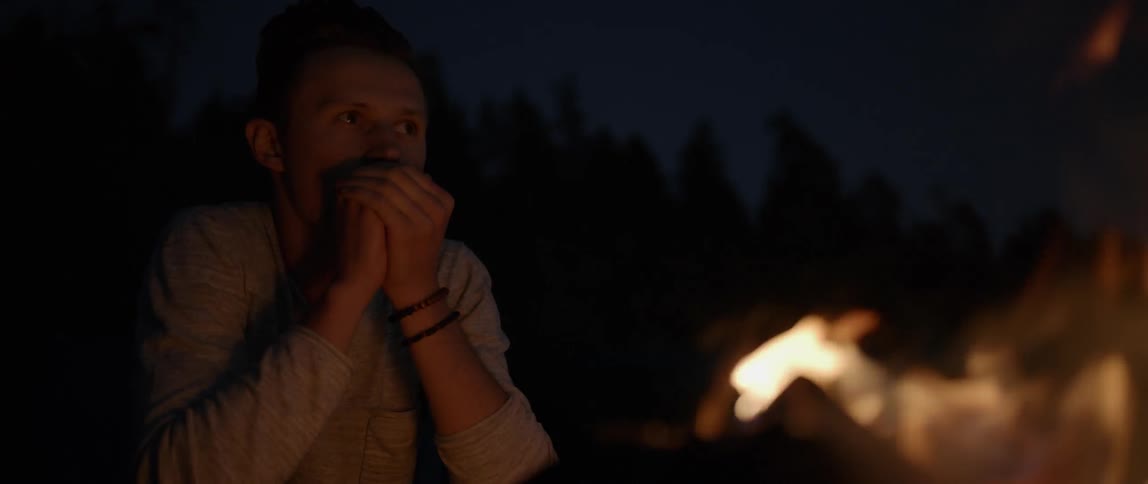 A man is warming his hands at a campfire at night