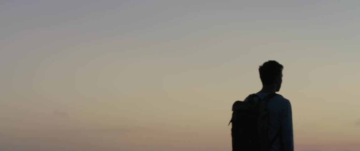 A man wearing a backpack walking forward with the sunset in the background