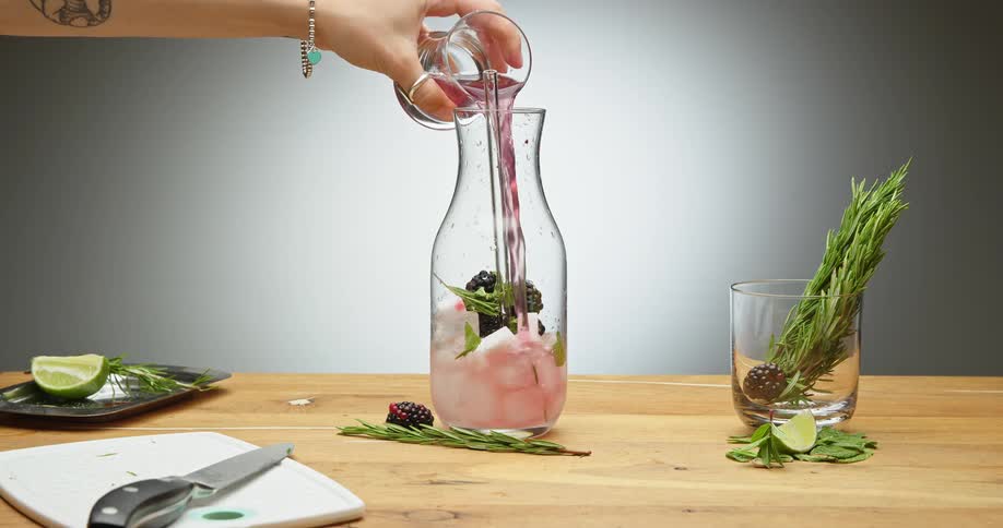 A person pouring a glass of red liquid into a jar on a table