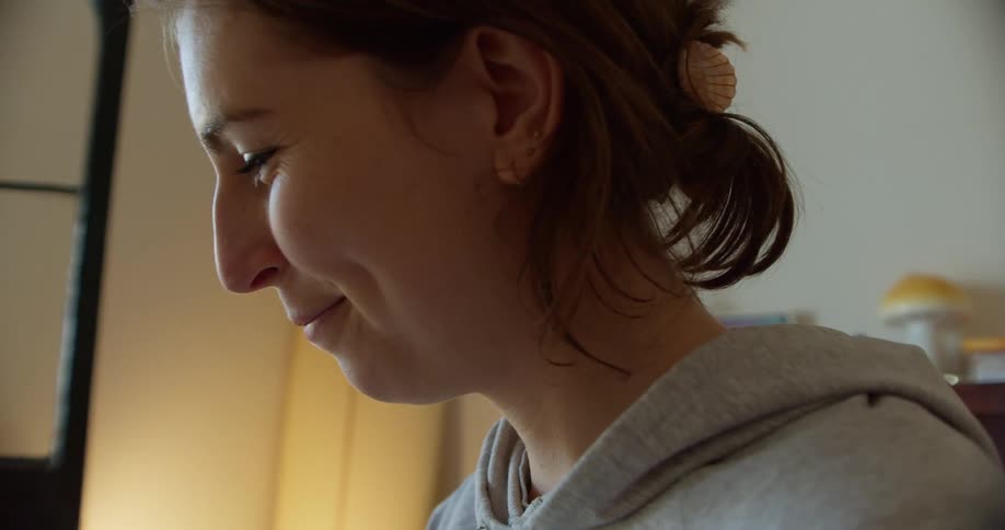 A young woman sitting indoors smiles and talks while looking at something out of frame