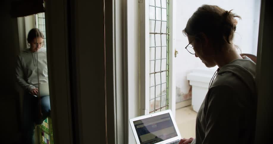 A young woman stands with her leg position outward to stabilize her laptop computer