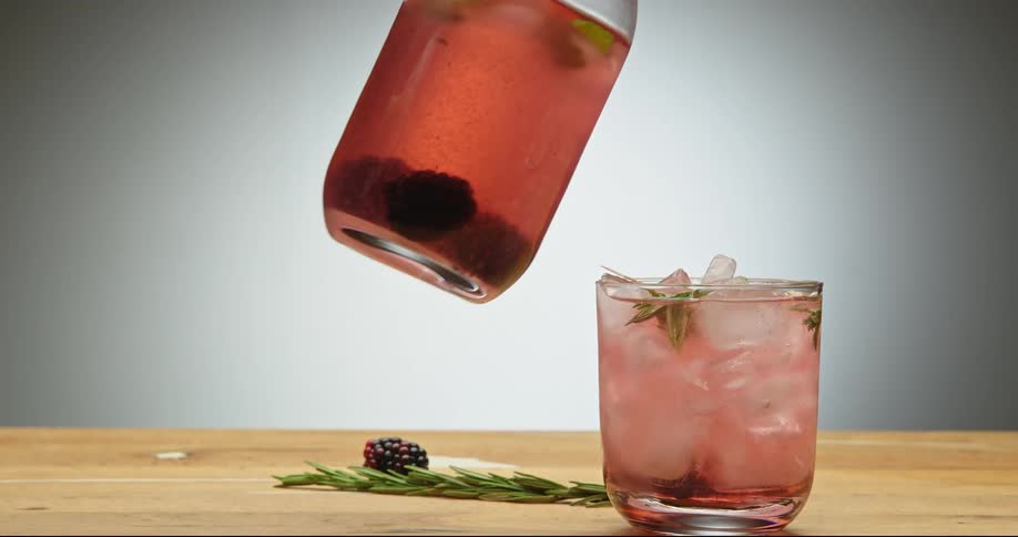 Pouring sangria from glass decanter into drinking glass and adding garnish
