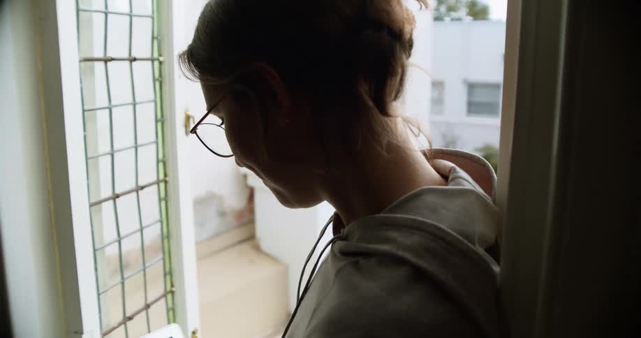 A woman with glasses sitting in a doorway typing on a laptop