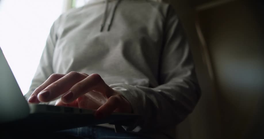 Woman with glasses and a grey hoodie uses a grey laptop