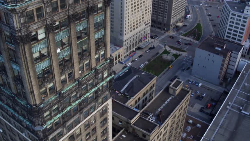 An aerial view of a tower in a city surrounded by high rises with cars driving on streets