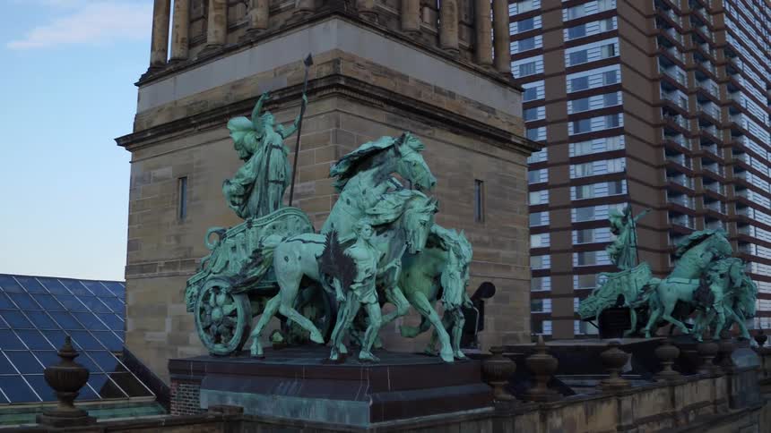 A statue on top of a building in a city with skyscrapers the sky and clouds in the background