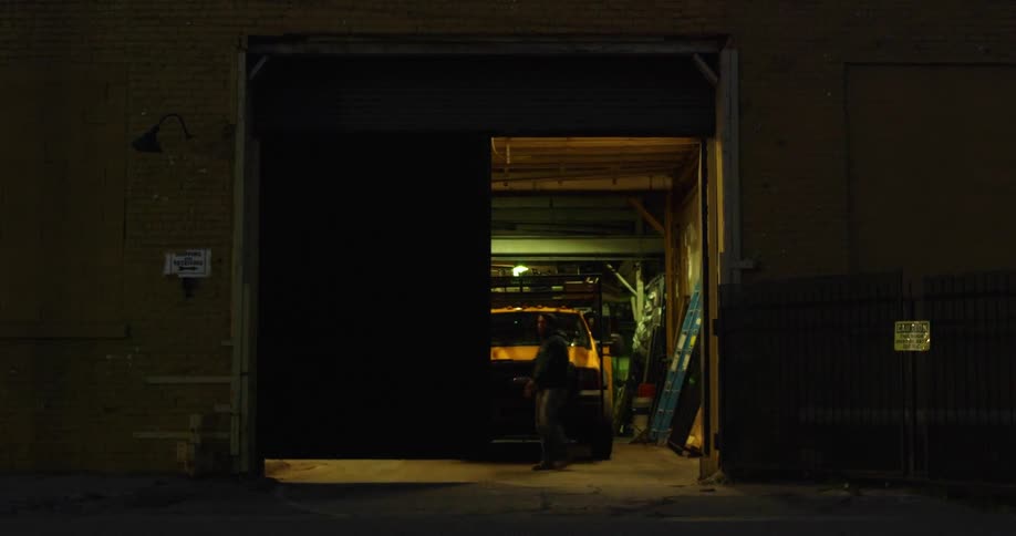 A man with a hoodie opening doors to a garage with a vehicle inside