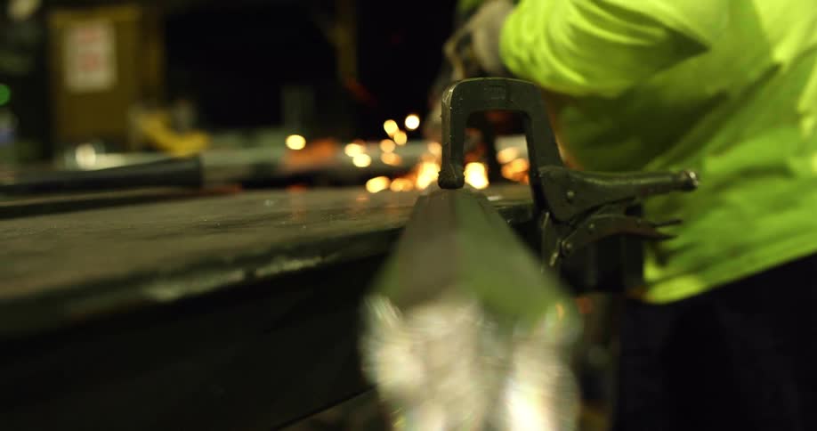 Person wearing protective gear uses power tool to polish metal bar creating sparks