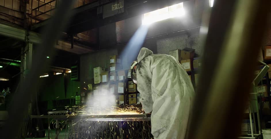 Worker wearing protective gear cuts metal with a power tool in a warehouse