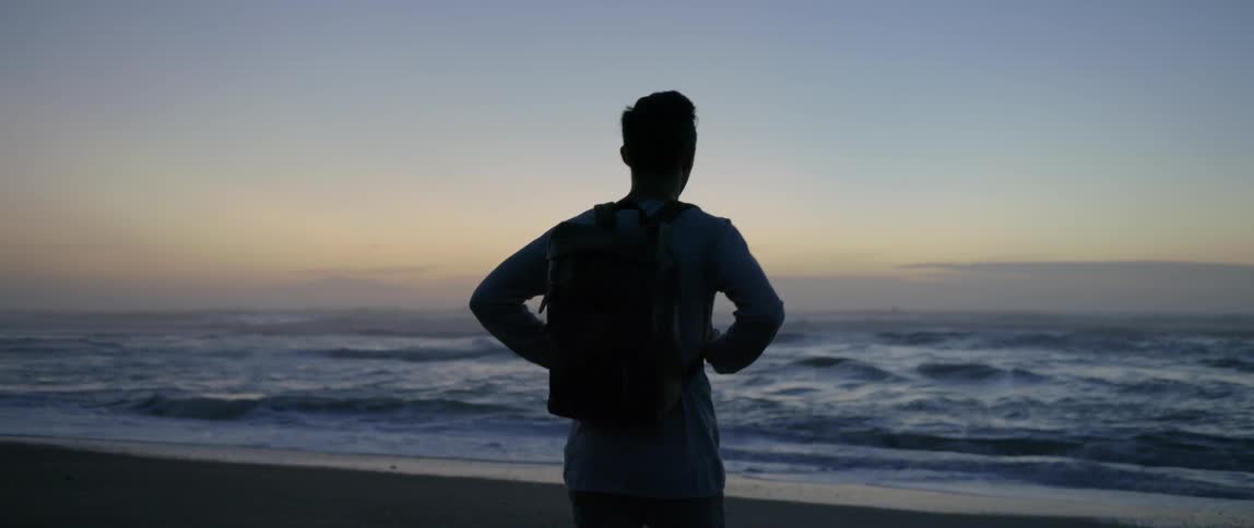 Man walking toward the ocean at sunset