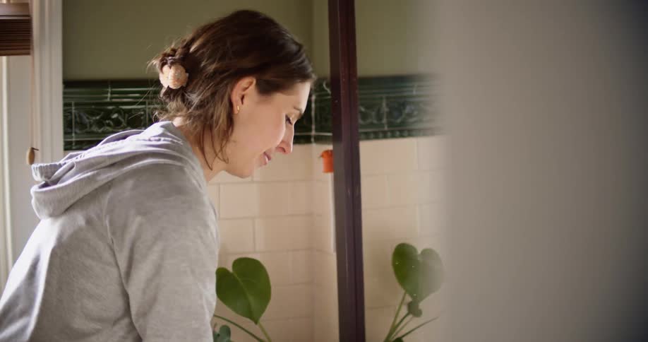 Woman with a grey hoodie and jeans washes her hands and dries them with a brown towel in the bathroom