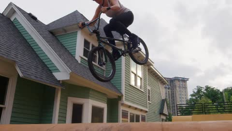 A girl on a bike jumps as she rides over a ramp in her back yard