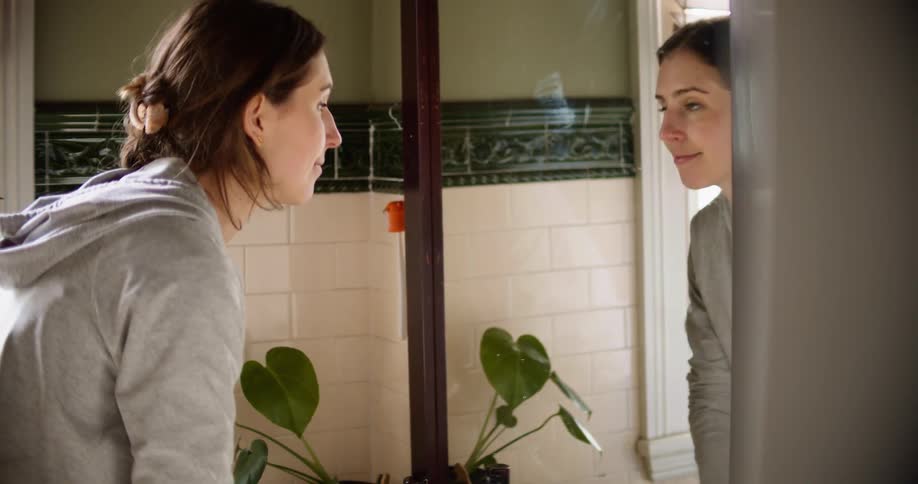 A woman in the bathroom washing her hands in a sink in front of a mirror