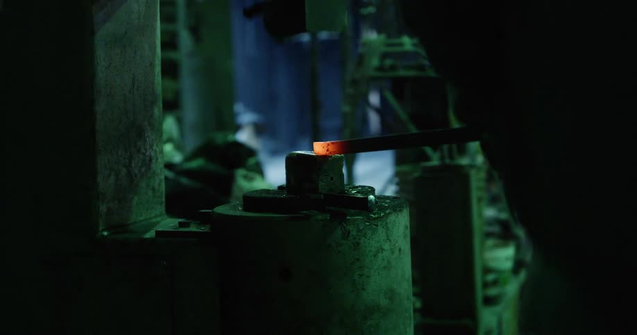 A pneumatic hammer shaping the hot tip of a metal rod in a foundry