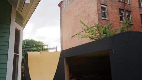 Woman rides bike along man made bike path including jump near apartment buildings