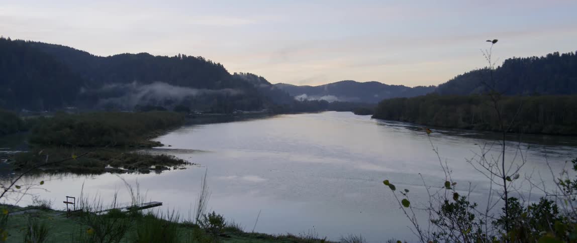 Wispy clouds hang in the air above a lake with mountains in the background
