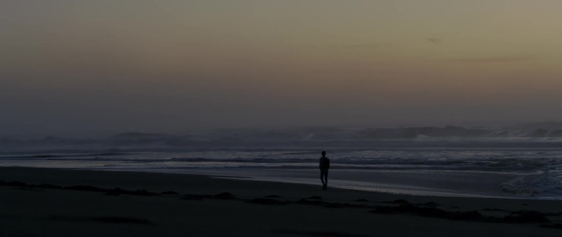 A man walks alone on a beach at dusk